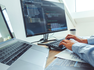 A person is typing on a keyboard in front of a computer.