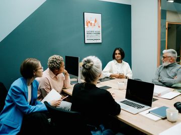 A group of people are sitting around a table with laptops.